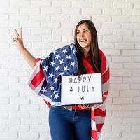 Mujer con bandera americana sosteniendo lightbox con palabras feliz 4 de julio foto