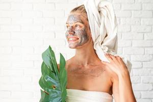 Woman with a clay facial mask holding a green monstera leaf photo