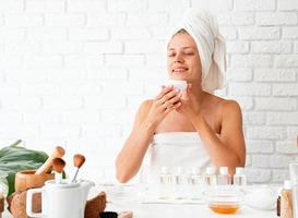 Woman in white bath towels smelling the cream doing spa procedures photo