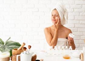 Woman applying cream on her face skin doing spa procedures photo