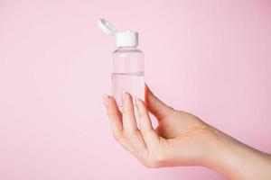 Hands with a bottle on pink background. Spa and body care concept. photo
