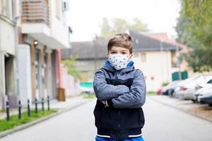 Little boy with arms crossed wearing kn95 face mask outdoors. photo