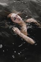 Young woman with raised arms in the water. Black water photo