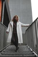 A girl with red curly hair in a white coat poses on the parking stairs