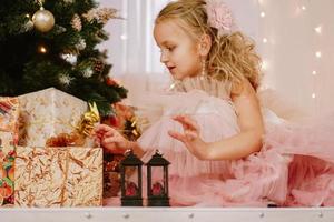 niña con un vestido rosa cerca del árbol de navidad