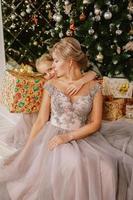 hija abrazando a su madre mientras está sentada en el árbol de navidad