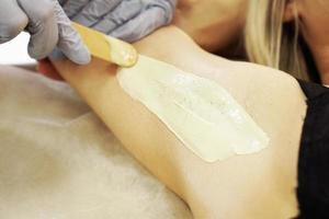 Waxing woman armpit with spatula. Salon wax beautician epilation photo