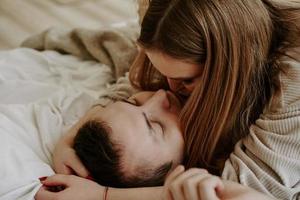 Close-up portrait of a beautiful young kissing couple in bed at home photo