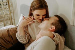 Close-up portrait of a beautiful young kissing couple in bed at home photo