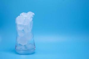 The ice in clear glass of water melting on blue background. photo