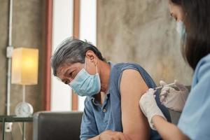 una doctora asiática está vacunando a un anciano en su casa.