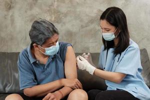 una doctora asiática está vacunando a un anciano en su casa.