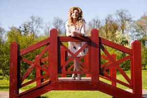 Beautiful woman in summer dress and straw hat stands on birch bridge photo