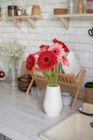 Red and pink gerbera daisies in a white vase on a wooden kitchen