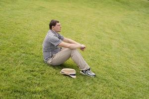 Young thoughtful man sitting on the grass in the park photo