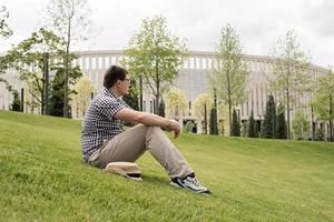 Young thoughtful man sitting on the grass in the park photo