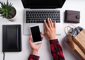 Woman hands working on laptop holding mobile phone, top view flat lay