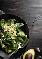 Top view of fresh summer avocado and spinach salad on black wooden photo