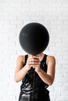 Woman in black dress holding black balloon in front of her face photo