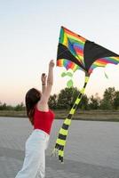 Mujer joven volando una cometa en un parque público al atardecer foto