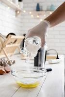 Pouring powder sugar into glass bow with eggs on white wooden table. photo