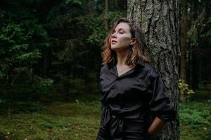 Young woman - close portrait in a dark forest. Woman in black shirt photo