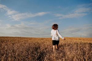 mujer corre en un campo de trigo en un día de verano. concepto de felicidad y alegría foto