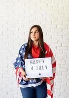 Mujer con bandera americana sosteniendo lightbox con palabras feliz 4 de julio foto