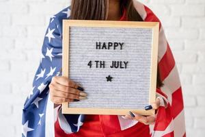 Mujer con bandera sosteniendo tablero de letras con palabras feliz 4 de julio foto