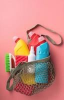 Botellas sanitarias y herramientas de limpieza en bolsa de malla sobre fondo de color rosa foto