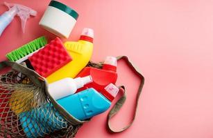 Sanitary bottles and cleaning tools in mesh bag on pink background photo