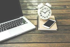 Laptop, notebook, smartphone and alarm clock on wooden table photo