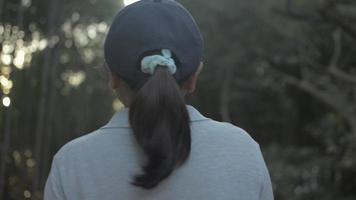 Rear view woman wears cap walking through a pathway in natural park video