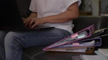 Mujer sentada y trabajando con un portátil y un montón de documentos en casa video