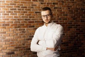 Handsome man with glasses standing near red brick wall photo