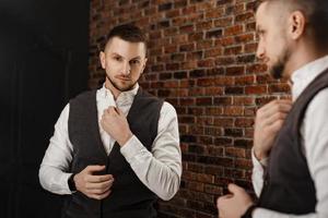 Stylish confident young man looking at himself in mirror photo