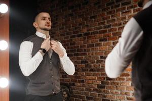 Stylish confident young man looking at himself in mirror photo