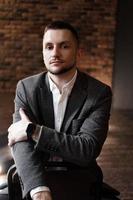 Handsome fashionable man in a white shirt sits on a chair in a studio photo