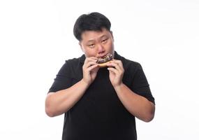 Joven gracioso hombre asiático gordo comiendo donas de chocolate foto