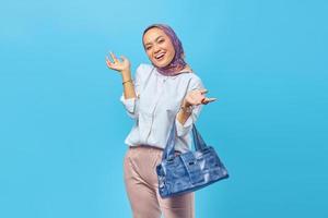 Cheerful young woman standing holding bag on blue background