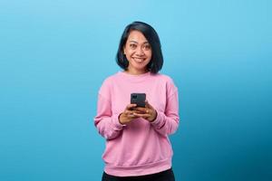 Hermosa mujer asiática sonriendo mediante teléfono móvil sobre fondo azul. foto