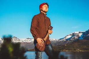 chico con una guitarra en el fondo de montañas, bosques y lagos foto