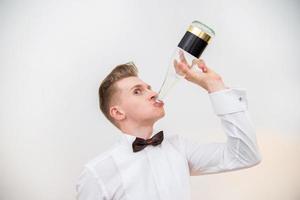 Joven bebiendo de una botella de vidrio sobre un fondo blanco. foto