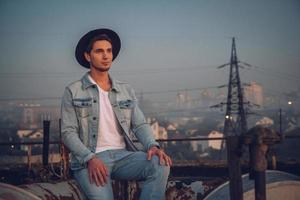 Hombre con sombrero vestido con camisa blanca y jeans en el fondo de la ciudad foto