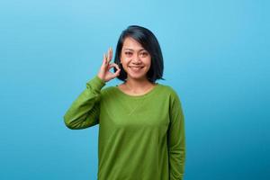 Beautiful Asian woman showing gesturing okay sign on blue background photo