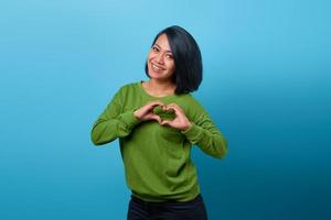 Portrait of smiling Asian woman showing heart gesture with two hands photo