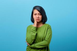 Asian woman touching cheek with bored expression on blue background