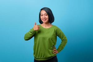 Sonriente mujer asiática mostrando los pulgares para arriba sobre fondo azul. foto