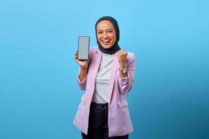 Mujer asiática mostrando la pantalla en blanco del teléfono inteligente y celebrando el éxito