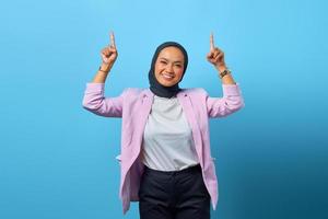 Retrato de mujer asiática alegre apuntando hacia arriba sobre fondo azul. foto